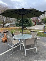 Full set displayed outside showing round glass top table with umbrella and four matching chairs.