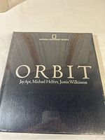 Front cover of National Geographic Orbit book showing navy blue padded leather cover with gold lettering, sealed in plastic wrap.