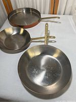 Set of three copper bottom pans with brass handles arranged on a white surface showing overall condition and size relation.