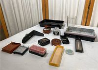 Photo showing a variety of vintage Polaroid photography accessories arranged on a white surface including storage trays, flashes, light meter and cases.