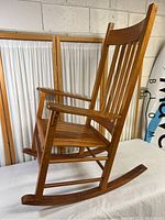 Side view of the solid wood rocking chair showing armrest, slatted seat and rocking supports on the floor.