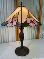 Front view of lamp showing Tiffany style stained glass shade with pink flowers and green leaves, and metal base.
