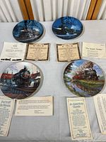 Overview of four decorative train collector plates laid flat, each accompanied by certificates of authenticity.