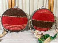 Two vintage round canteens side-by-side, showing red and brown striped fabric covers and attached cloth straps.