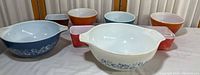 Full view of eight Pyrex bowls and dishes in various colors and sizes on table