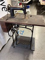 Full side view of sewing machine mounted on wooden table with treadle base showing overall condition and wear