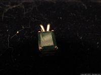 Photo showing a close-up of a 14K gold pendant with a rectangular emerald gemstone held by four prongs.