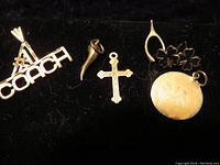 Photo shows six distinct 14K gold charms arranged on a black background: a Coach logo with teepee design, a curved horn, a cross with ornate edges, a wishbone with three four-leaf clovers, and a round locket with light engraving.