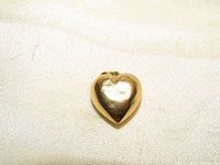 Close-up of a small 14K yellow gold puffed heart charm with a loop for attachment, placed on a light fabric background.