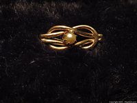 Photo of 14K gold infinity symbol pin with a pearl in the center on a dark background.
