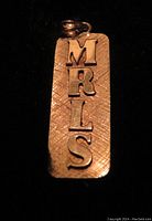 Front view of rectangular 14K gold pendant showing raised letters MRLS vertically arranged.