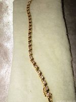 Full length view of tennis bracelet on cream-colored fabric showing the entire length of the gold-tone S-link chain with embedded clear stones.
