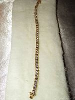 Full length image of tennis bracelet laid flat on cream cloth showing gold-tone metal and clear stones.