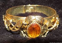 Close-up front view of the gold-tone bangle bracelet highlighting oval yellow stone and leaf decoration