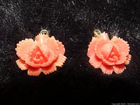 Front view of two coral rosebud flower pendants on black fabric background, showing intricate carving and color.