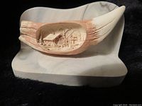 Carved bear tooth replica with detailed scene of cabin and trees carved inside, on a smooth base