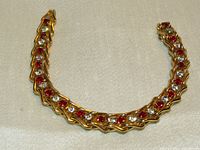 Top view of gold bracelet showing alternating white and red stones set in gold with a curved design.