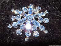 Close-up image of vintage layered snowflake brooch pin with ice blue round and baguette rhinestones prong set, showing sparkle and detail on dark background.