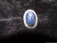 Close-up photo of an oval blue lapis stone with gold veining set in a handmade sterling silver bezel ring with a rope-like border.