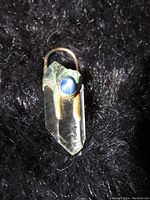 Close-up photo of a 14K gold pendant containing a clear crystal and a blue star sapphire gem on a black background.