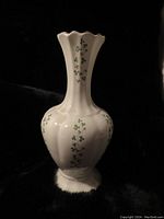 Full view of the white fluted vase with green shamrock decoration and gold rims on top and bottom, against a black background.