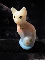 Front and side view of the opaque glass stylized cat figurine with hand-painted pink floral decoration and blue base on black background.