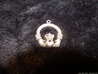 Front side of sterling silver Irish Claddagh charm showing crowned heart held by two hands on black background.