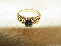 Close-up of the front view of the ornate gold ring with a deep blue oval sapphire in the center, showing the intricate gold band details.