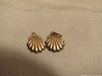 Close-up photo of a pair of 14k gold shell-shaped earrings placed on fabric surface.