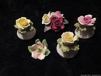 Five floral porcelain pieces including three salt and pepper shakers with rose tops, miniature flower figurine, and floral bouquet figurine on black background