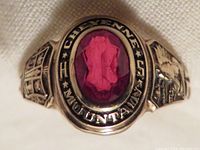 Close-up photo showing the front of the vintage 1971 Cheyenne Mountain High School class ring with oval faceted ruby and inscription.