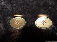 Pair of oval cufflinks showing star design with diamonds and green enamel on gold background.