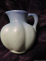 Front angled view of the turquoise matte blue pottery small pitcher showing the bulbous shape and handle.