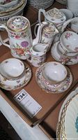 Full view of assorted porcelain coffee pots, cups, saucers, and plates in floral pattern with gold trim.