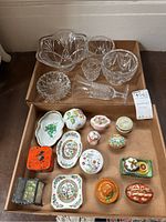 Top view of all glass bowls, wine glass, and multiple porcelain trinket boxes and dishes laid out in a cardboard box.