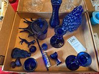 Top down view of the full collection of cobalt blue glass items arranged in a cardboard box showing various figurines, glassware, and decorative pieces.