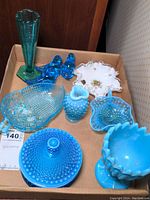 Full view of the box with various blue glass items including tall green vase, two blue bird figurines, clear blue patterned dish, hobnail lidded dish, starburst shaped dish, and acorn dish