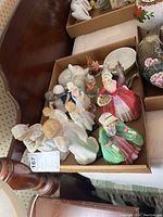 Box of assorted porcelain figurines including female figures, rabbit and bird figurines, and small decorative pieces.