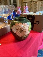Front view showing pink hibiscus flower and green leaves on dark green round vase.