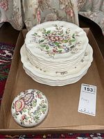 Stack of floral Royal Doulton dinner and luncheon plates alongside a round ceramic floral patterned paperweight in a cardboard box on a patterned rug