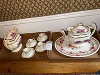 Wide shot showing the teapot, 4 teacups and 4 saucers arranged on cardboard trays