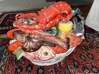 Top angle view showing the large bright red lobster, various fish and lemon slice on seafood tureen lid with detailed textures and paint.