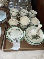 Overview of six Spode Christmas Tree cups, six matching saucers, and a decorative bell with matching green and holiday motif on white china.