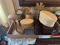 Overview photo showing various wooden storage boxes, jewelry boxes, framed pictures, and a figurine placed inside a cardboard tray.
