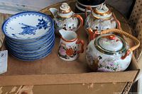 Overview photo showing the set of blue and white plates stacked, two teapots, sugar bowl, and creamer arranged on a cardboard surface.