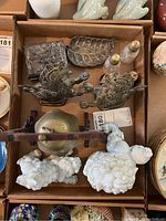 Overview of various items in lot including two white ceramic Asian lion figurines, smaller dark metal lions, a brass bell in a wooden frame, metal leaf dish, metal trinket box and two ceramic salt and pepper shakers.