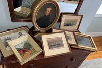 Grouped display of framed artworks and mirror on a wooden dresser showing the contents of the lot