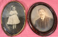 Overview of both antique oval bowed glass portraits side by side showing brass and mahogany frames on pink background.