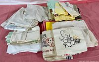 Photo showing multiple stacks of folded antique linens including table cloths and napkins with some featuring embroidered cartoon-like bear designs.