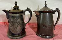 Two large Victorian silver-plated ice pitchers displayed side by side, showing overall size and design differences.